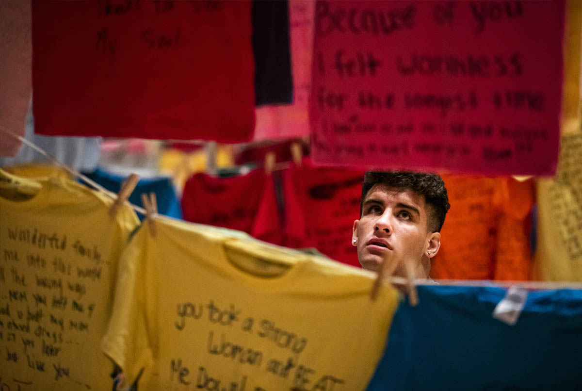 A UVU student reads the messages written by survivors on multi-colored t-shirts.
