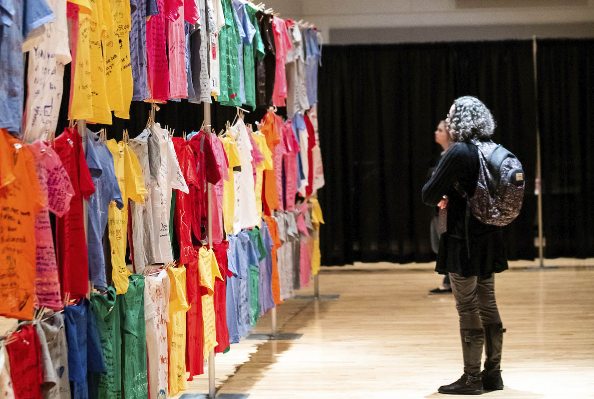 Students read a wall of colorful t-shirts decorated by survivors of domestic abuse at the Clothesline Project at Utah Valley University.