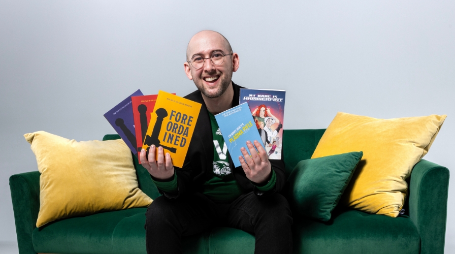 Student seated on a sofa, holding books.