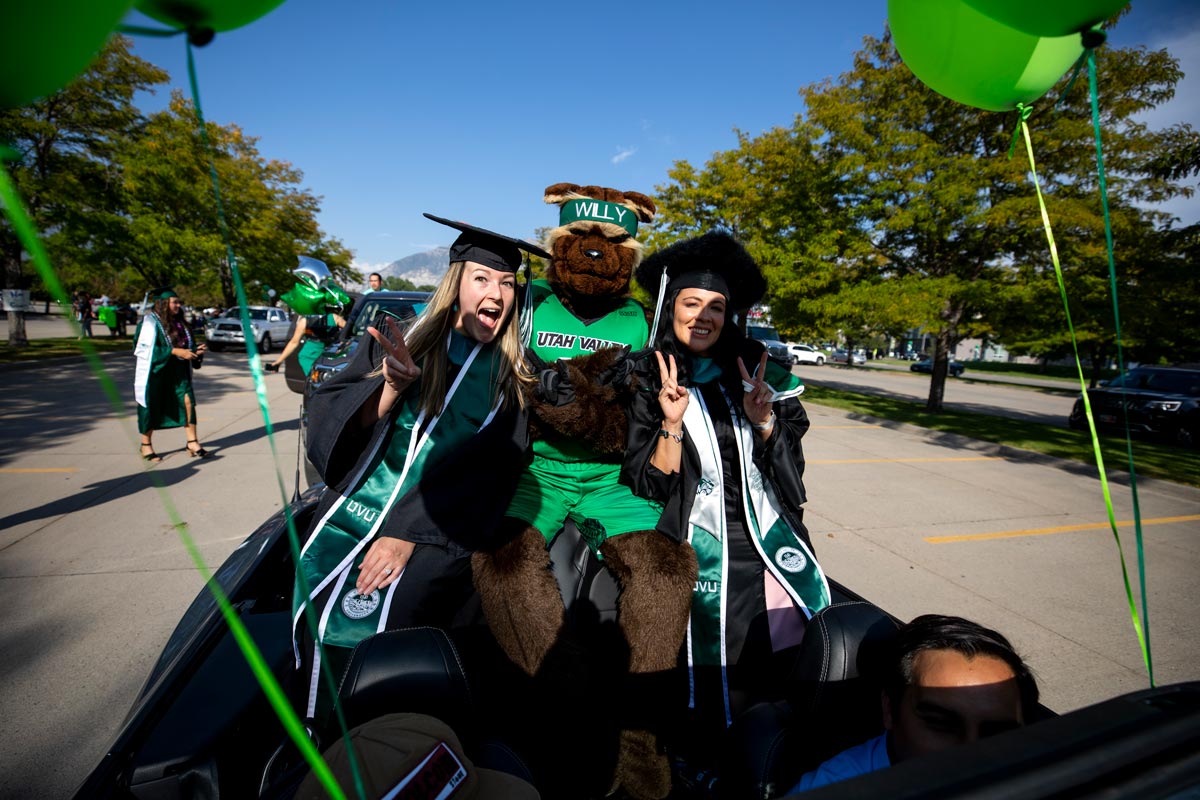 Two new grads pose with mascot Willy