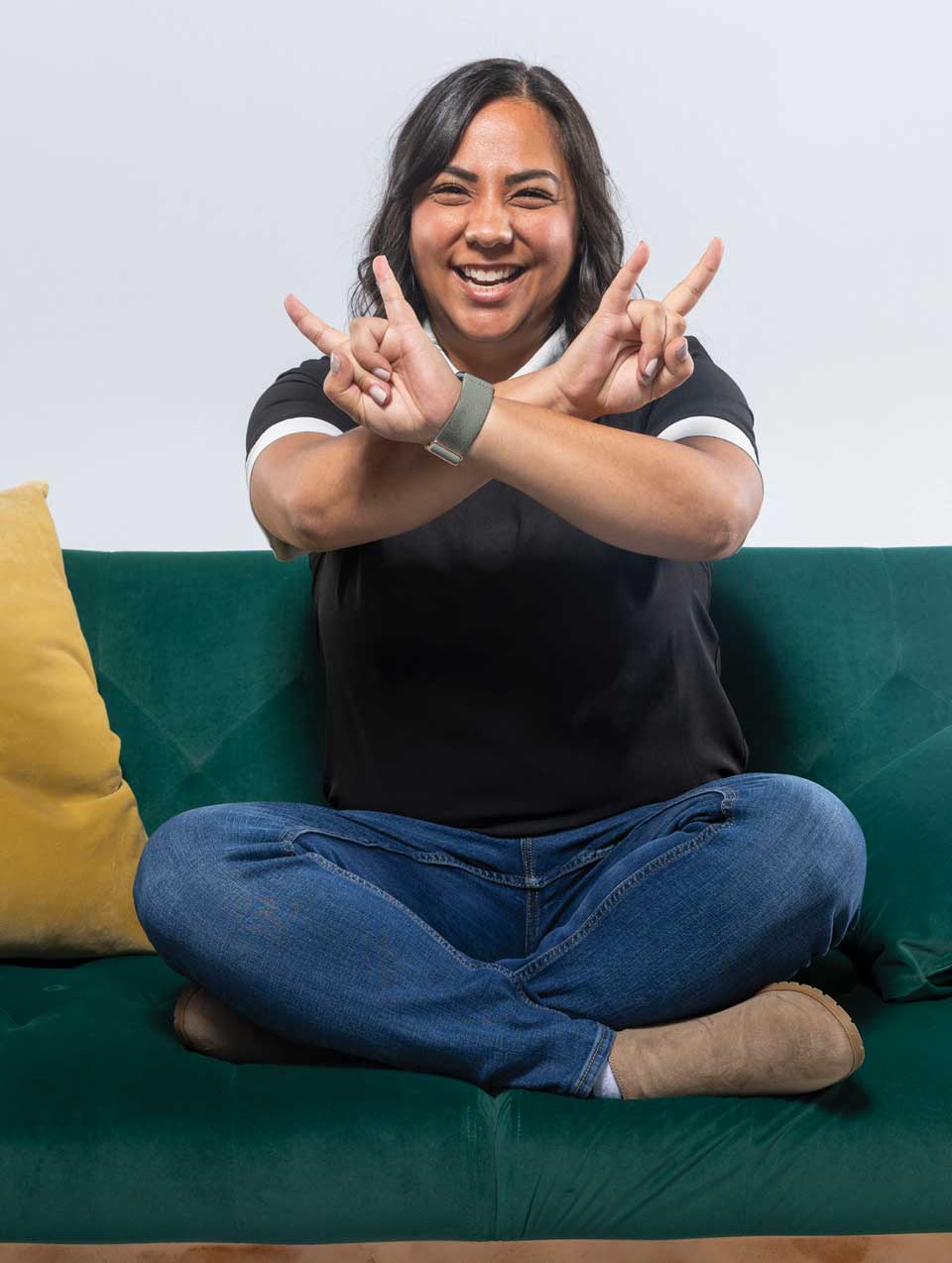 Kiana McAllister makes UVU hand symbol while sitting on a green couch.