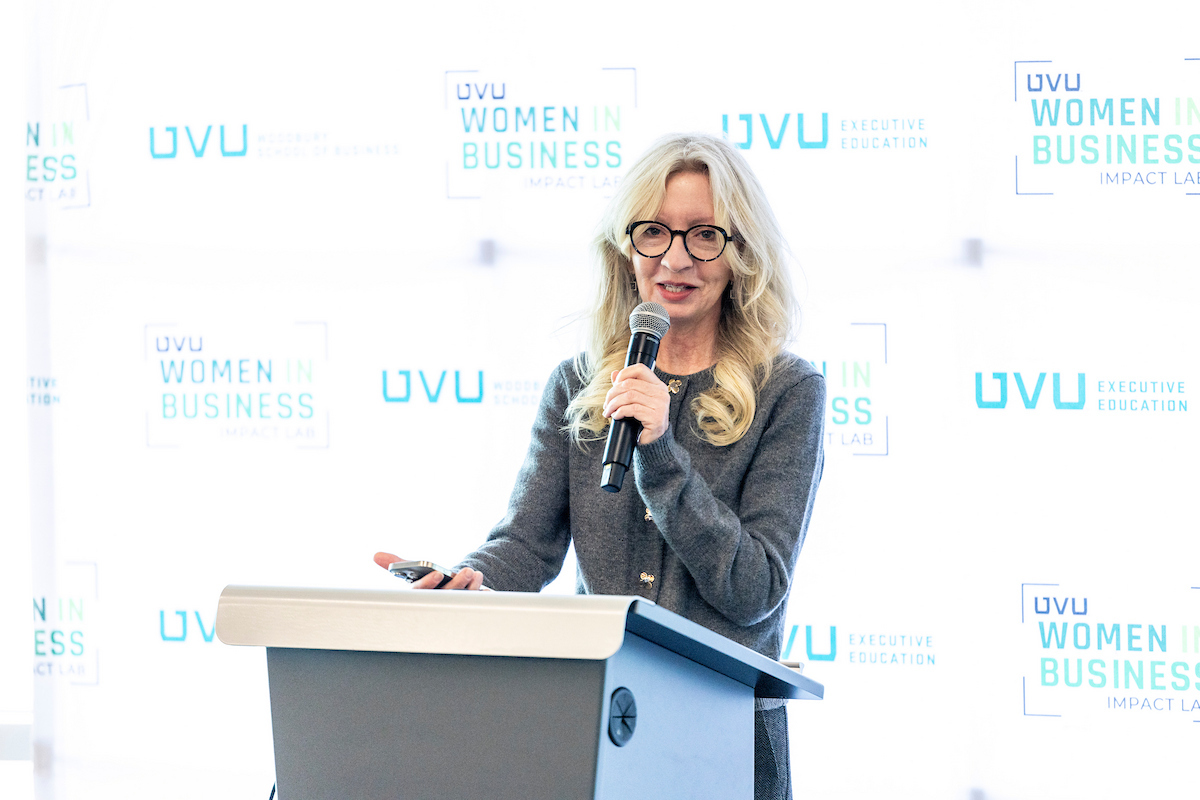 Dr. Maureen Snow Andrade speaks at a UVU Business Impact Lab event, standing at a podium with a microphone.