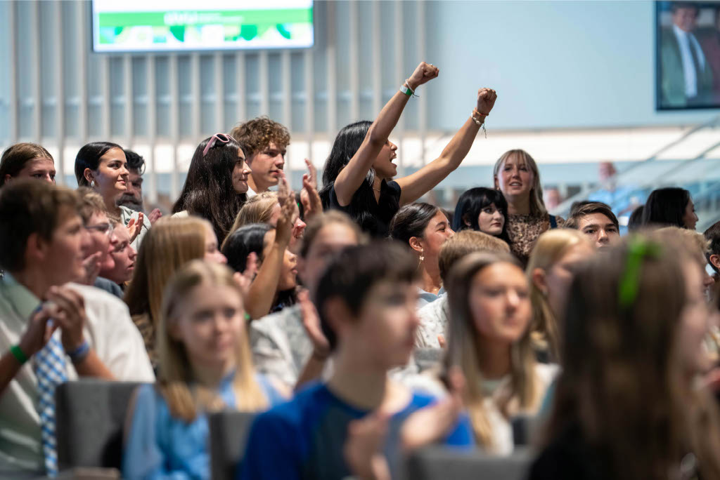 A student in a large audience raises her arms and cheers during the Alan Hall Marketing and Sales Invitational at UVU.