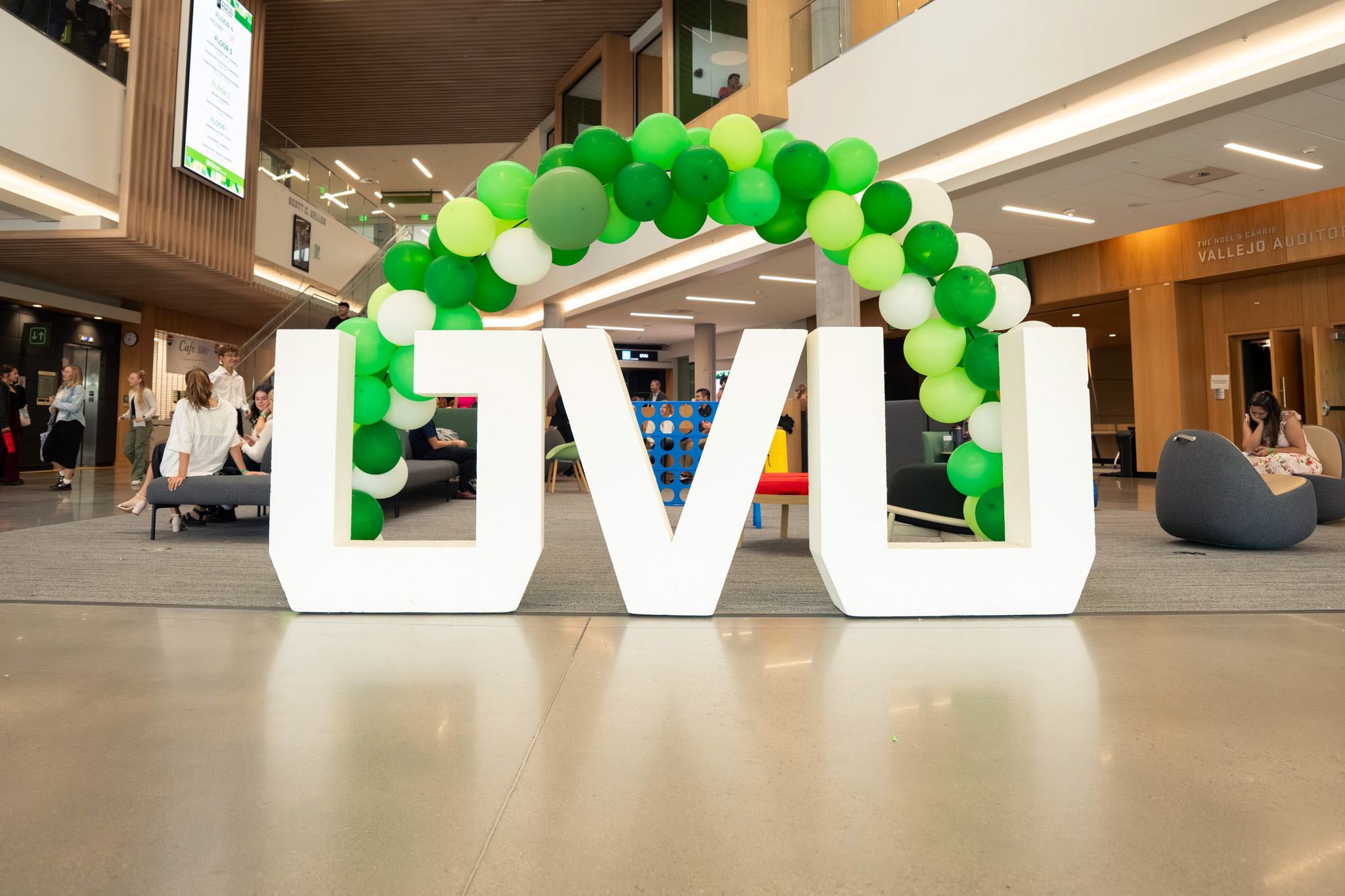 A large "UVU" statue in front of a green and white multicolored balloon arch in the foyer of the Scott C. Keller Business Building during the Alan Hall Marketing and Sales Invitational at UVU.