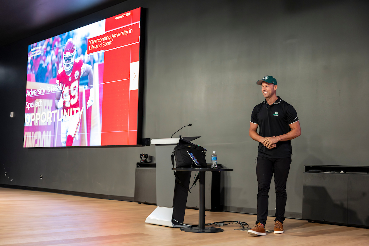 Daniel Sorensen stands on stage at UVU’s Keller Building, delivering his talk “Overcoming Adversity in Life and Sport” with a presentation slide showing his NFL career highlights.