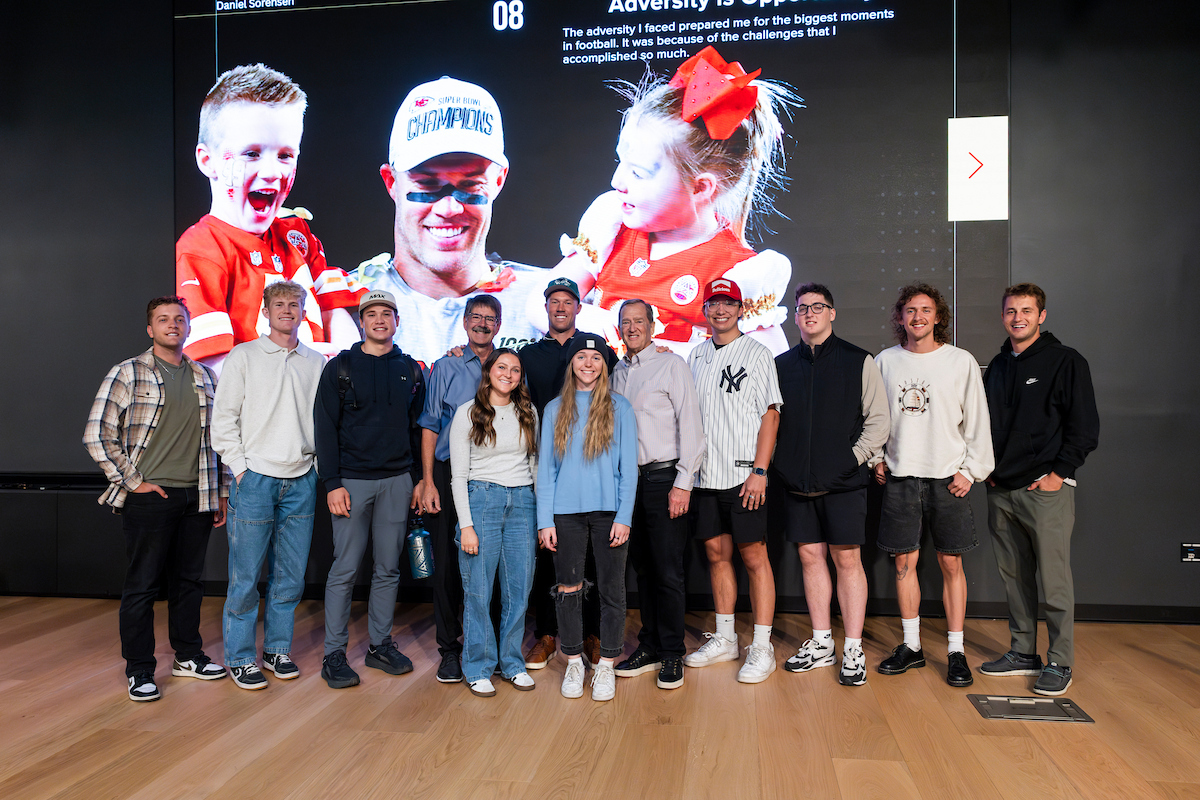 Daniel Sorensen poses with UVU students after his Halladay Lecture, smiling in front of a presentation slide featuring his Super Bowl win.