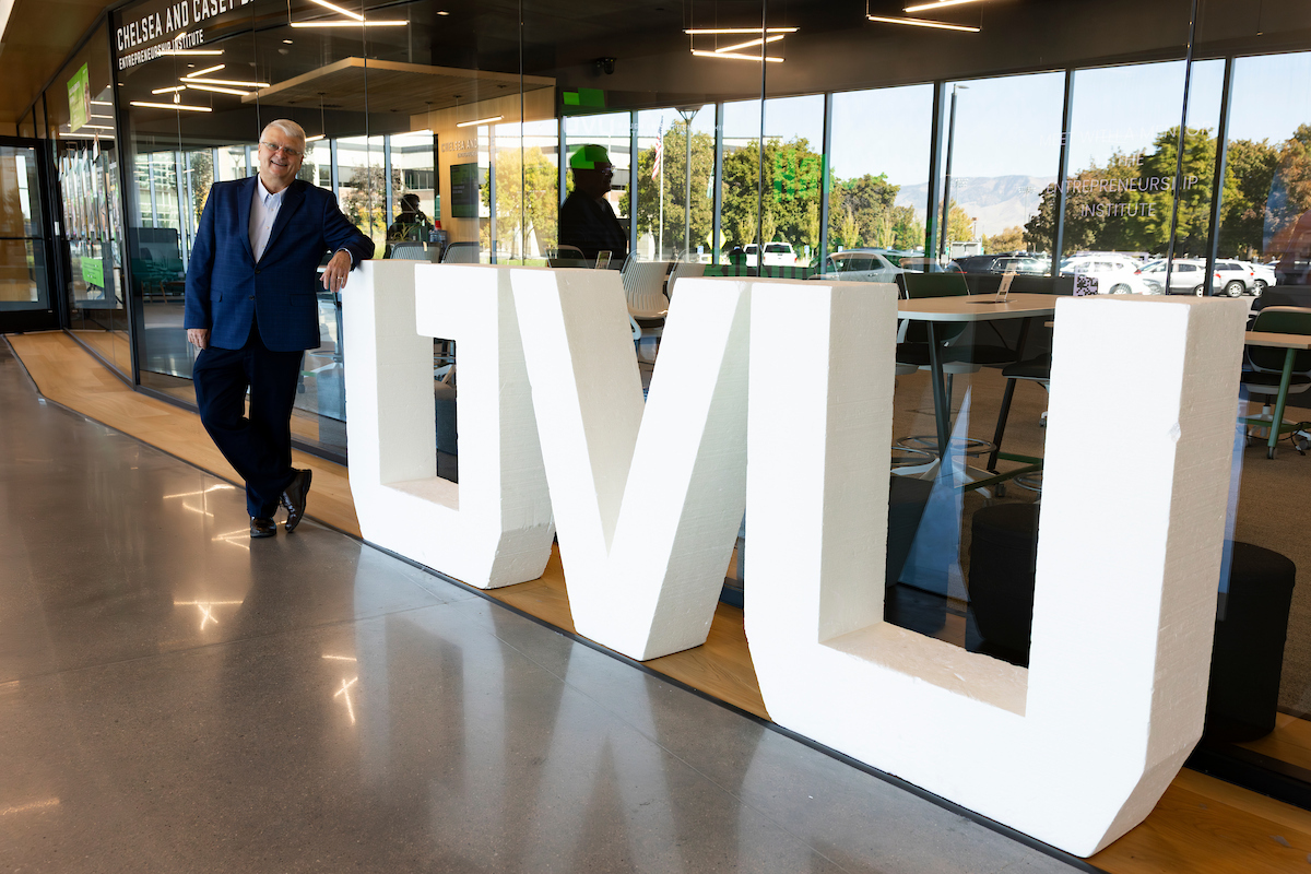 Guy Woodbury leans against large UVU letters inside the Keller Building, smiling after his Halladay Lecture.