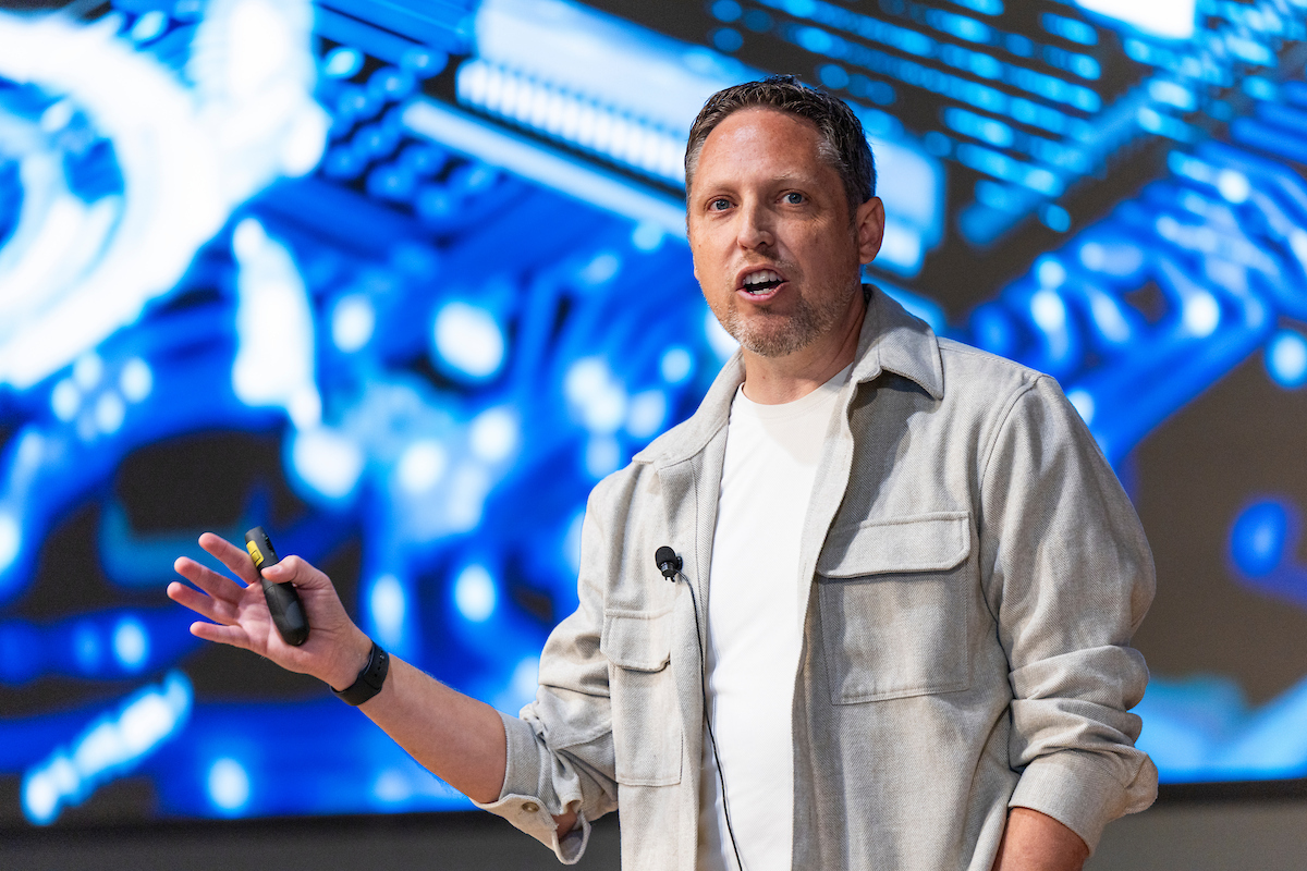 Sean Kennedy speaking on stage in front of a digital graphic background.