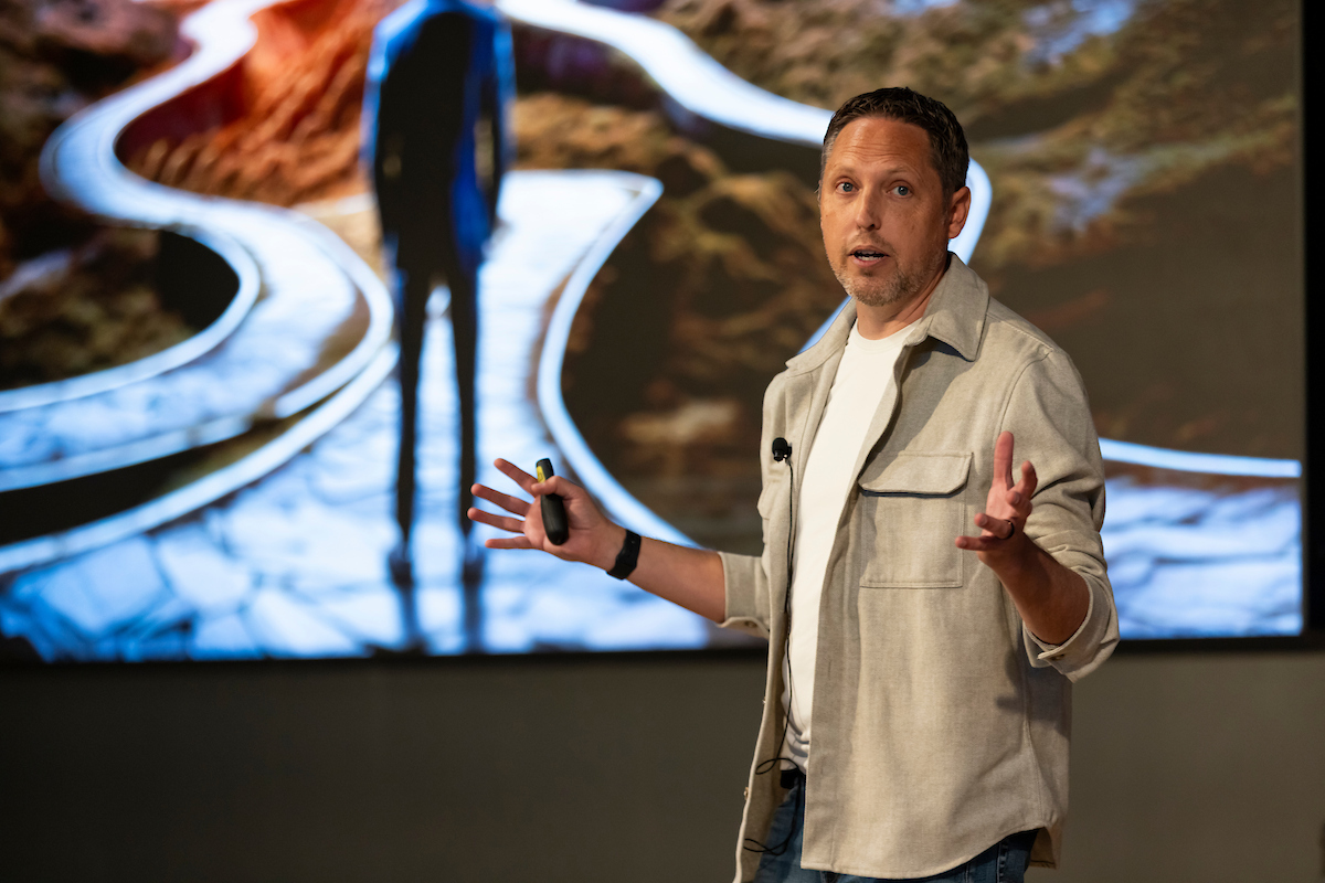 Sean Kennedy presenting on stage with a slide showing a person standing at a fork in the path.