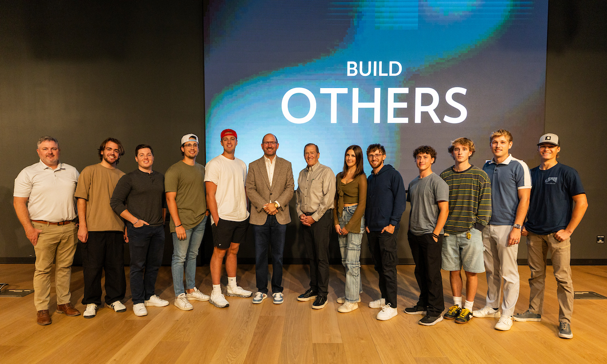 Brad Bonham stands with UVU students and faculty in front of a large “Build Others” screen after his lecture.
