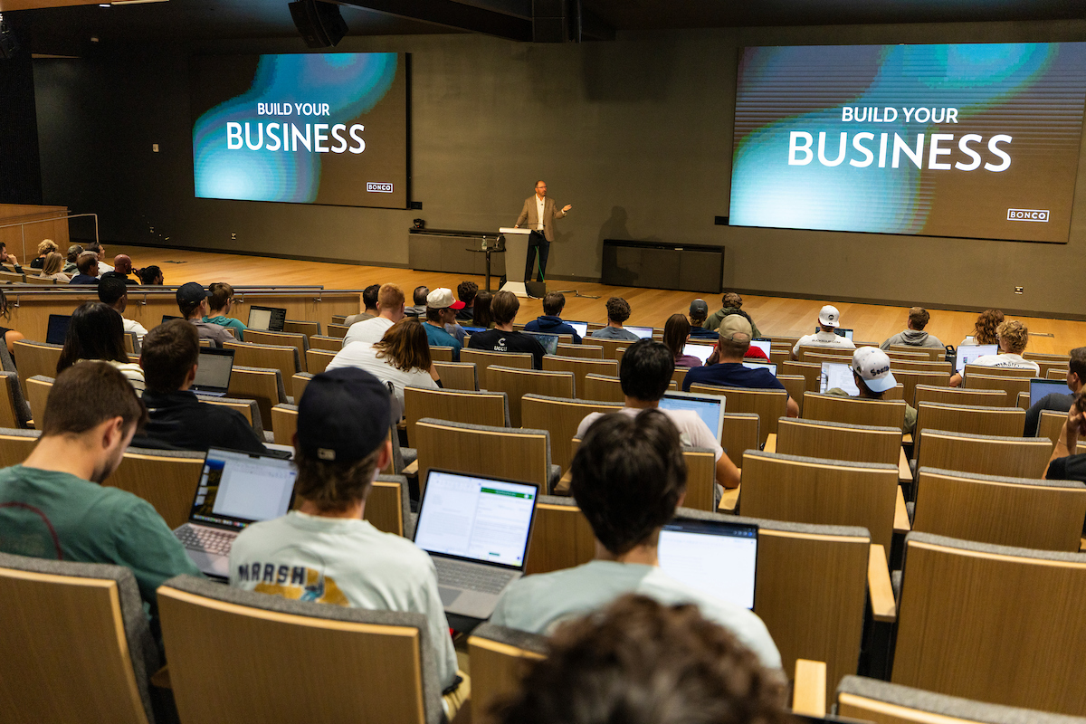 Brad Bonham speaks to UVU students in the Keller Building auditorium under a large screen that reads “Build Your Business.”