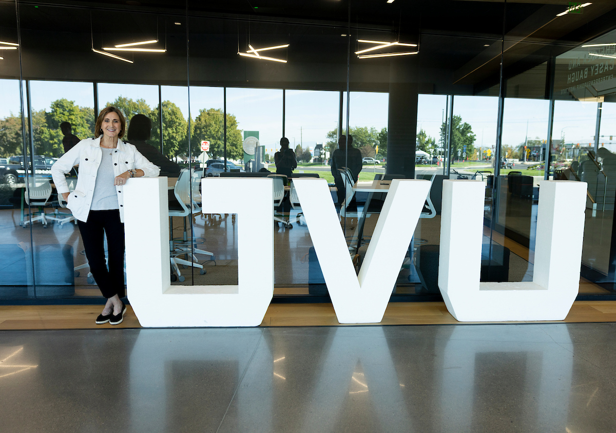 Kathie Lindemann, former Starbucks and Panera executive, stands beside large UVU letters in the Keller Building at Utah Valley University.
