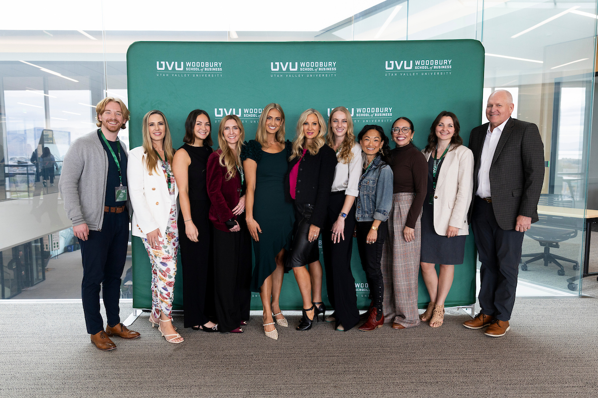 Group of UVU Woodbury School of Business staff and speakers posing together in front of a green event backdrop.