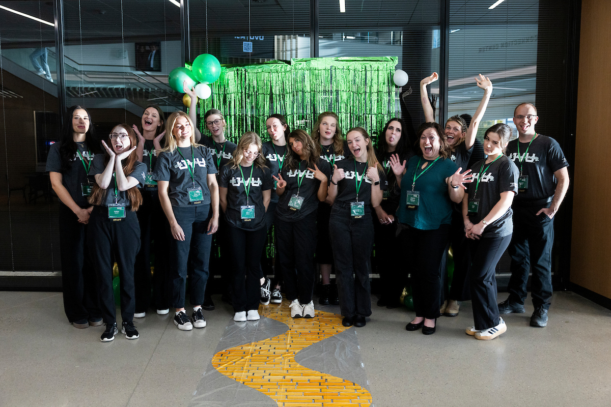 RISE conference student staff posing playfully in front of a green photo backdrop decorated with balloons.