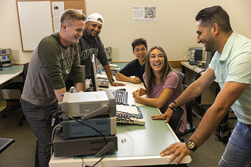 Students gathered around a table with electronic equipment on the table