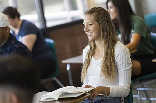 A student sitting in a classroom with a book open on their desk