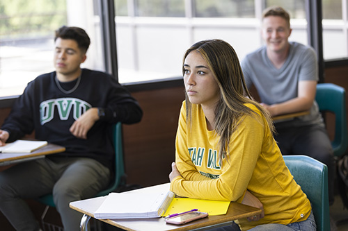 A student sitting in a classroom with a book open on their desk