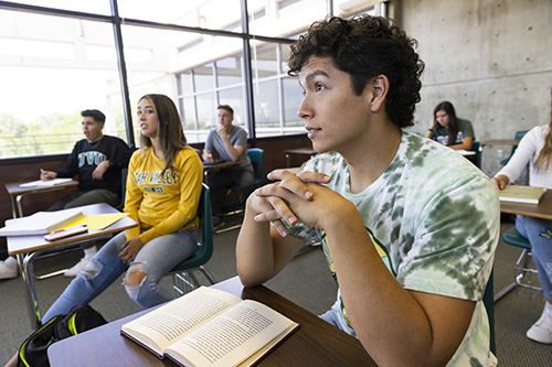 A student sitting in a classroom with a book open on their desk