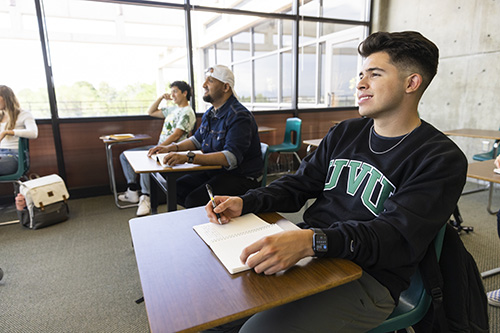 A student sitting in a classroom with a book open on their desk