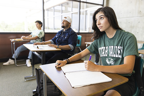 A student sitting in a classroom with a book open on their desk