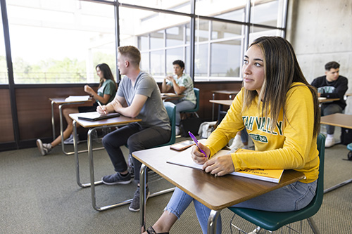 A student sitting in a classroom with a book open on their desk