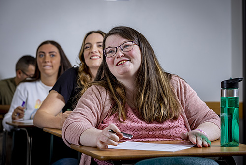 A student sitting in a classroom with a book open on their desk