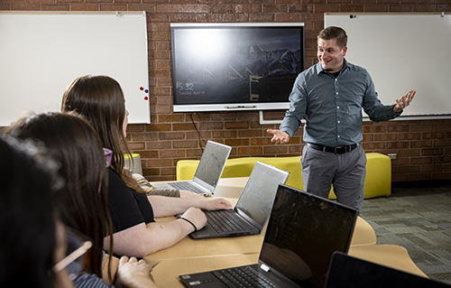 A teacher instructing students while they have laptops on their desks