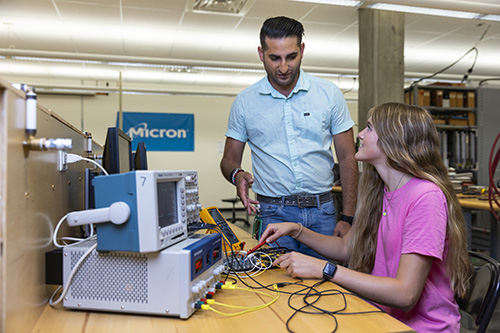 Professor and student use oscilloscope and other electronic tools.