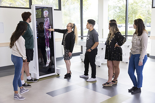 Students being instructed by a teaching pointing at a six foot tall tablet