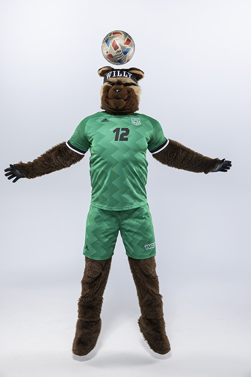 Willy the Wolverine wearing a green soccor uniform and bouncing a soccor ball on his head