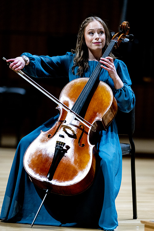 Student in blue dress plays the cello.