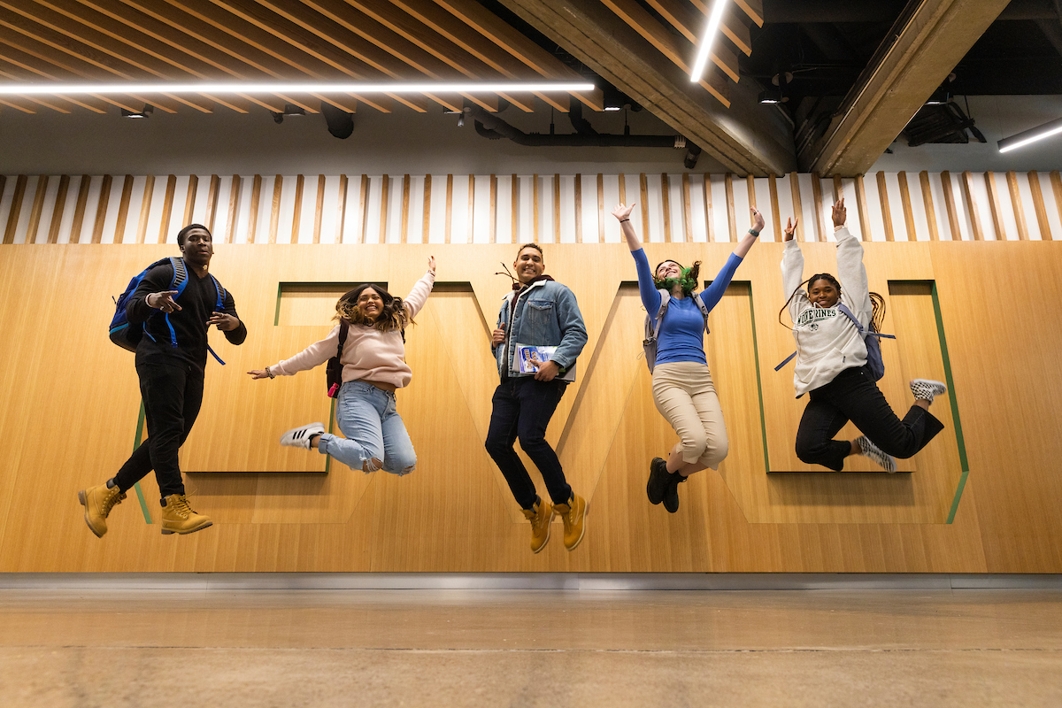 Students leap in the air in front of UVU wall feature.