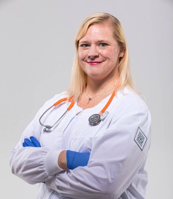 A woman smiles at the camera in a nurses uniform with her arms crossed