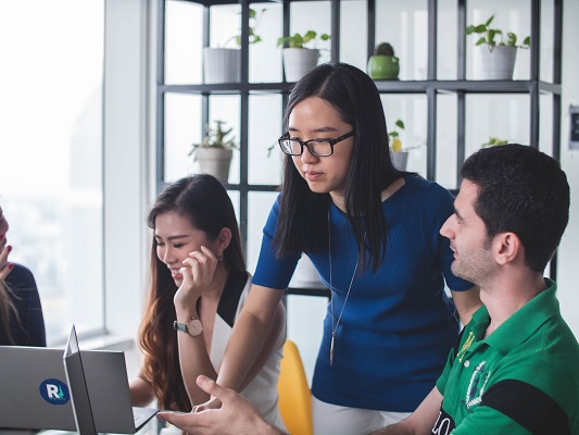 Woman leans over a computer and points a finger while students look on