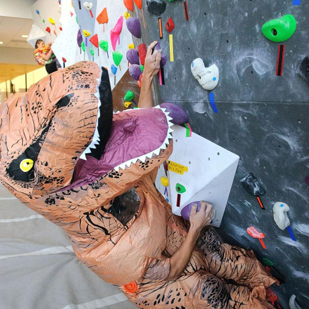 Person in dinsaur costume climbing at indoor climbing gym