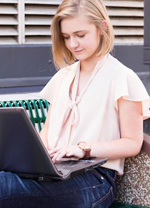 Girl working on laptop while seated on a bench.