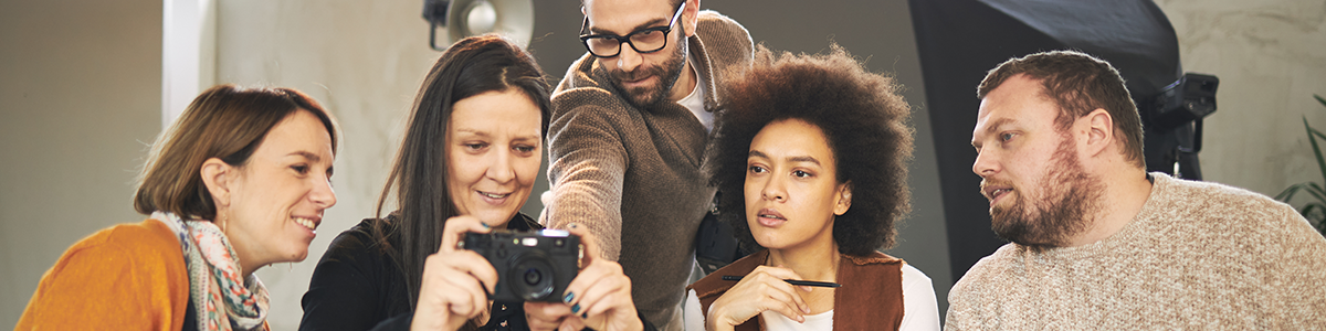 group of men and women looking at a camera as a man standing behind points at the camera