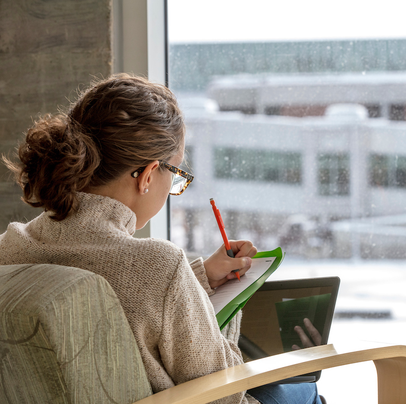 back of female student studying on a laptop in front of a window