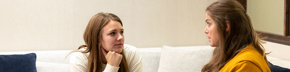 Two women sitting on a couch talking with each other.