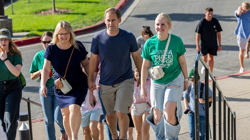 A student walking with her parents up some stairs with other people walking up behind them.