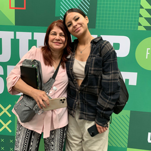 Two women stading next to each other with one arm around each other smiling at the camera standing in front of a backdrop with 'Jump Start' written on it. 