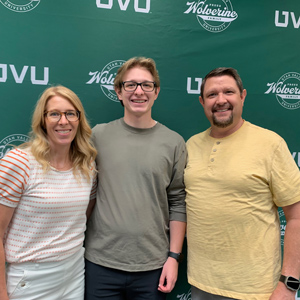 Parents standing on either side of their son standing in front of a UVU backdrop smiling at the camera.