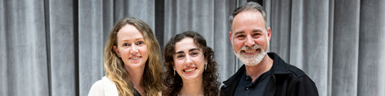 Parents standing on both sides of their daughter smiling at the camera