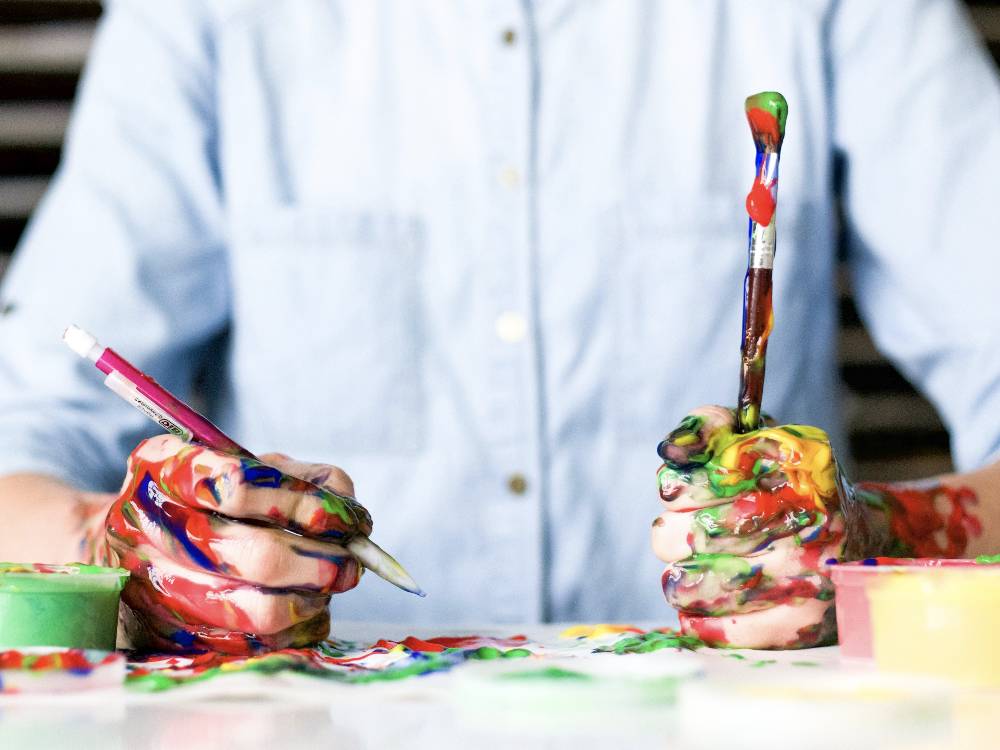 Hands covered in paint holding art supplies