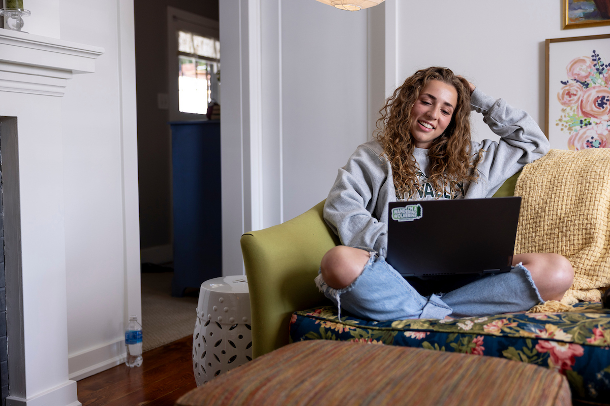 Person sitting on their couch at home, with their laptop in front of them.