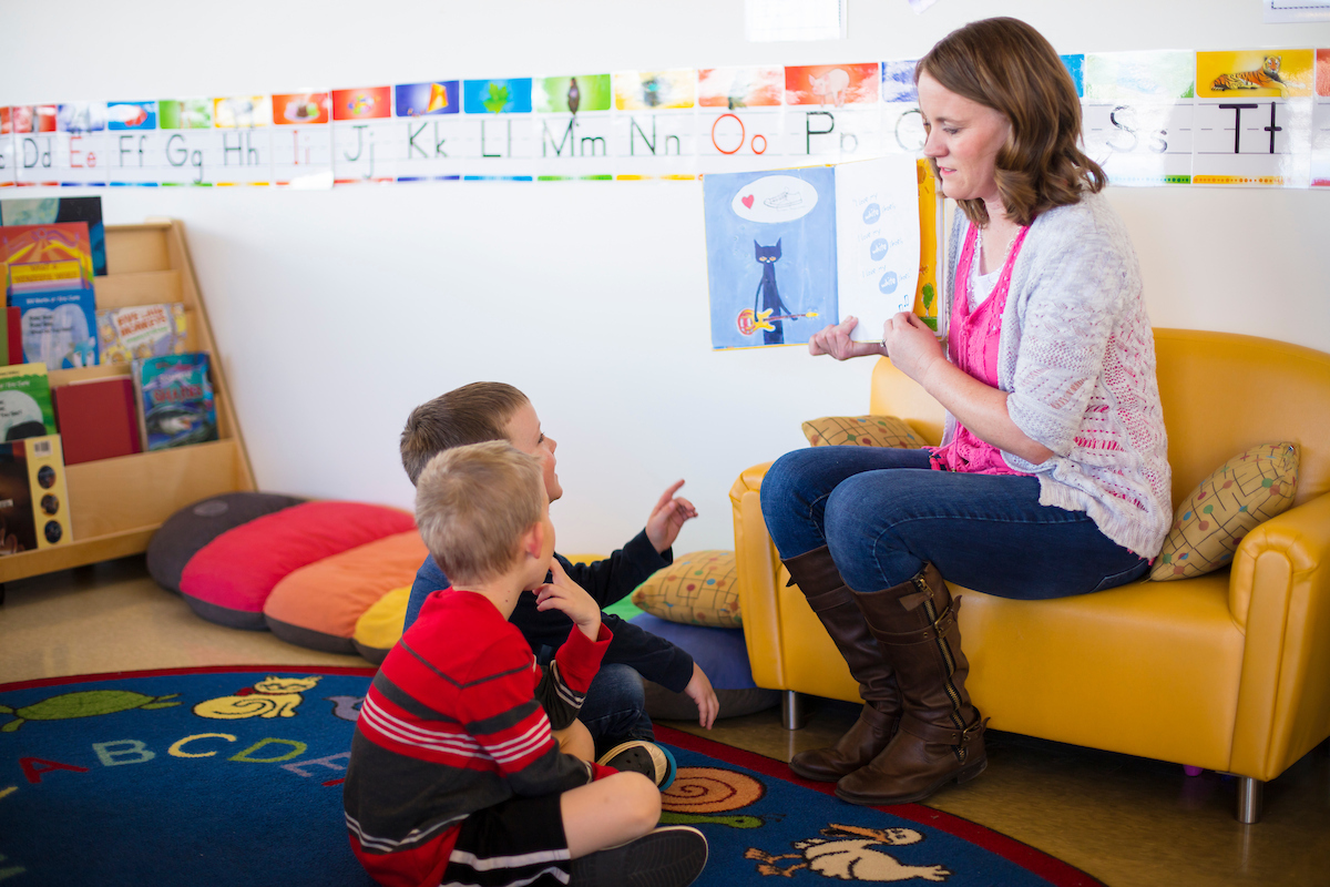 Elementary school teaching reading a book in front of their students.