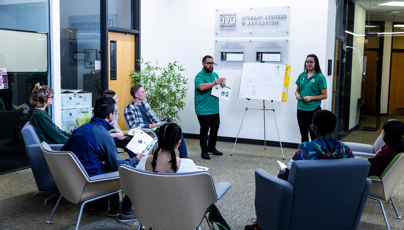 Two people standing in front of a chart, providing training to a group of seated employees.