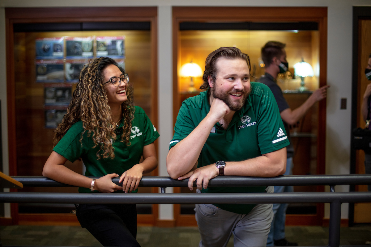 A female and a male employee leaning on a banister, laughing.