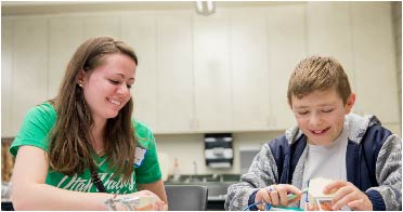 Student sits with child at a table teaching him how to brush his teeth