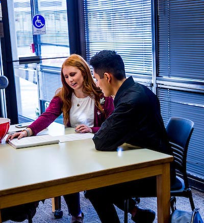 A woman and a man sitting at as desk, talking and pointing at a paper on the desk.